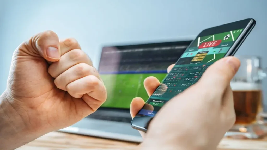 Giocatore analizza dati e statistiche sul laptop per una corretta gestione del bankroll nelle scommesse sportive, con smartphone e app scommesse sul tavolo